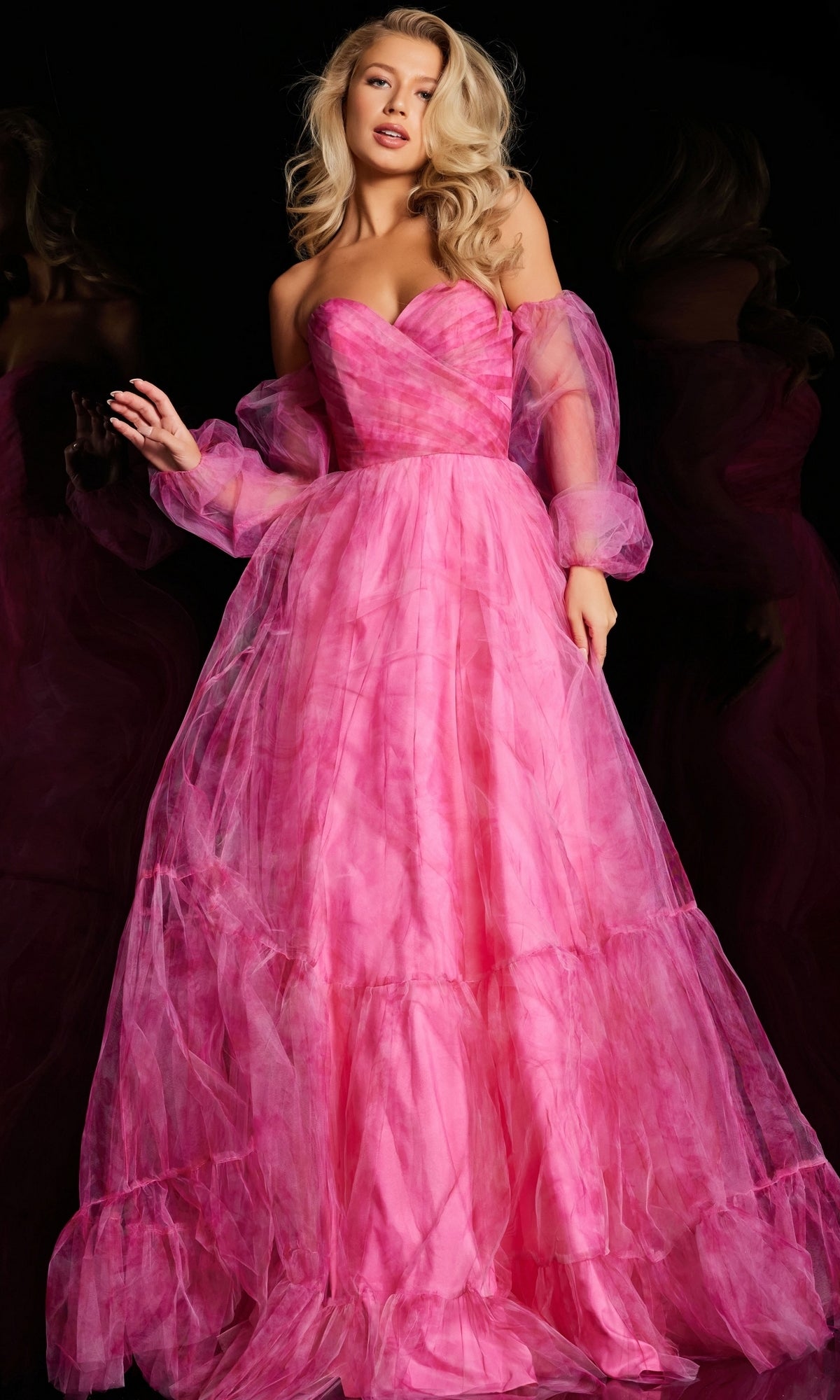 A woman models the Jovani Long-Sleeve Long Pink Formal Dress 38605, featuring sheer, puffy sleeves and a strapless neckline, set against a black background.